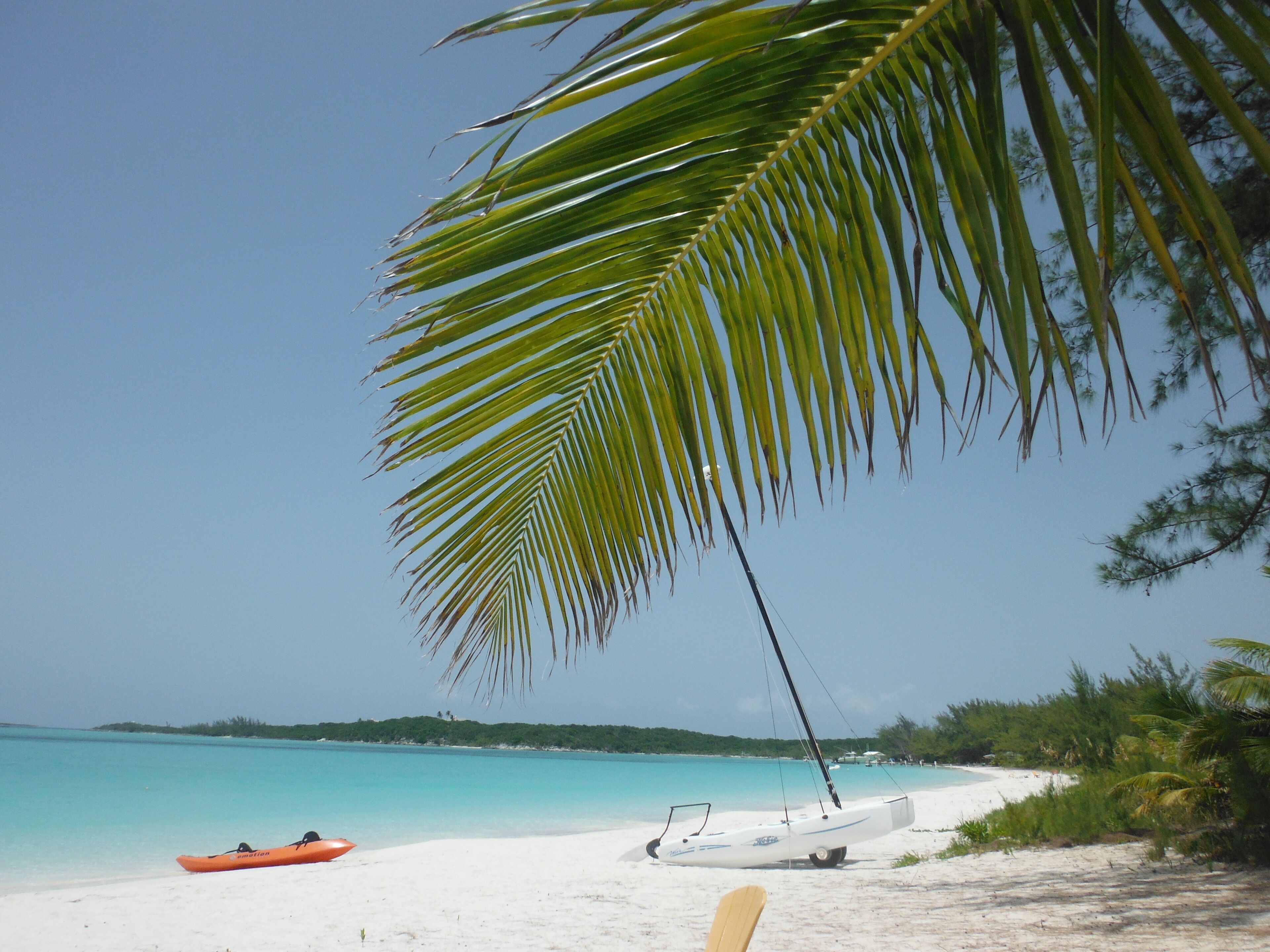 Una playa con orilla de arena blanca, un bote pequeño y un kayak rojo.