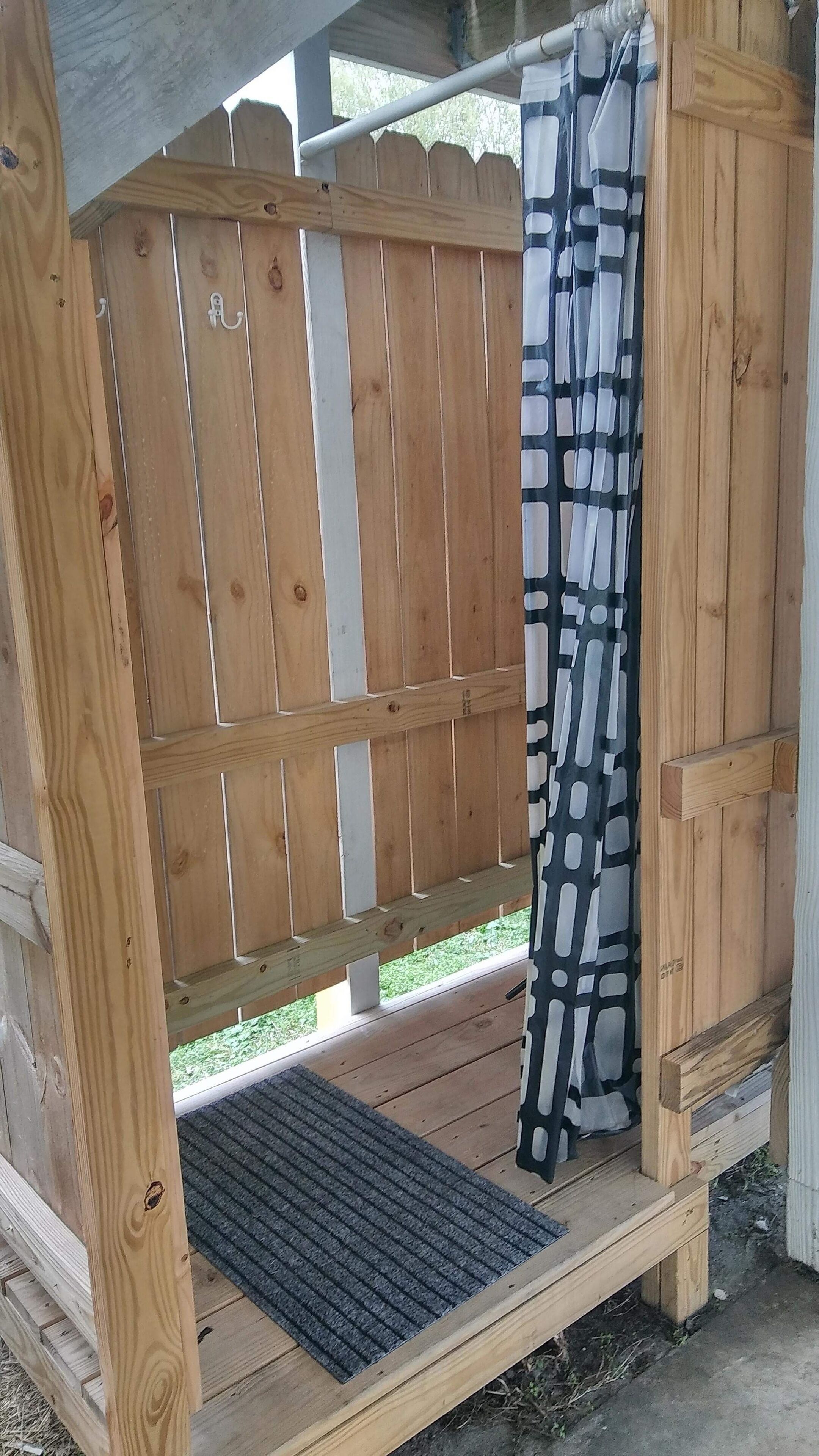 Une terrasse en bois avec un banc, un rideau à motifs noir et blanc et un paillasson.