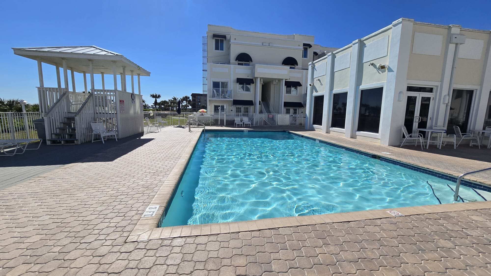 Une piscine dotée d’une zone couverte, un bâtiment avec de nombreux balcons et une terrasse dallée.