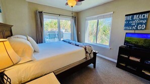 A bedroom with a bed, a TV, and a window with a view of palm trees.