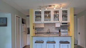 Una cocina con armarios blancos, encimera de granito y tres taburetes de bar.
