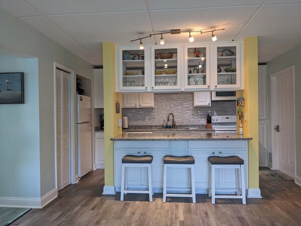 A kitchen with white cabinets, a granite countertop, and three bar stools.