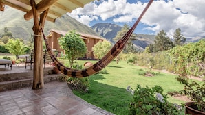 Un hamac sous une pergola en bois, une terrasse avec des meubles d’extérieur et une vue sur les montagnes et un jardin.