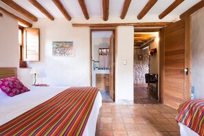 Ein Zimmer mit zwei Betten, Holzbalken, einer Steinwand und einem durch eine offene Tür einsehbaren Badezimmer.