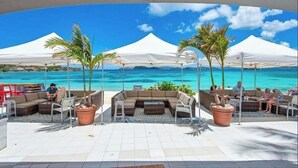 Eine Strandbar mit Außenbestuhlung, weißen Sonnenschirmen und Blick auf das Meer.