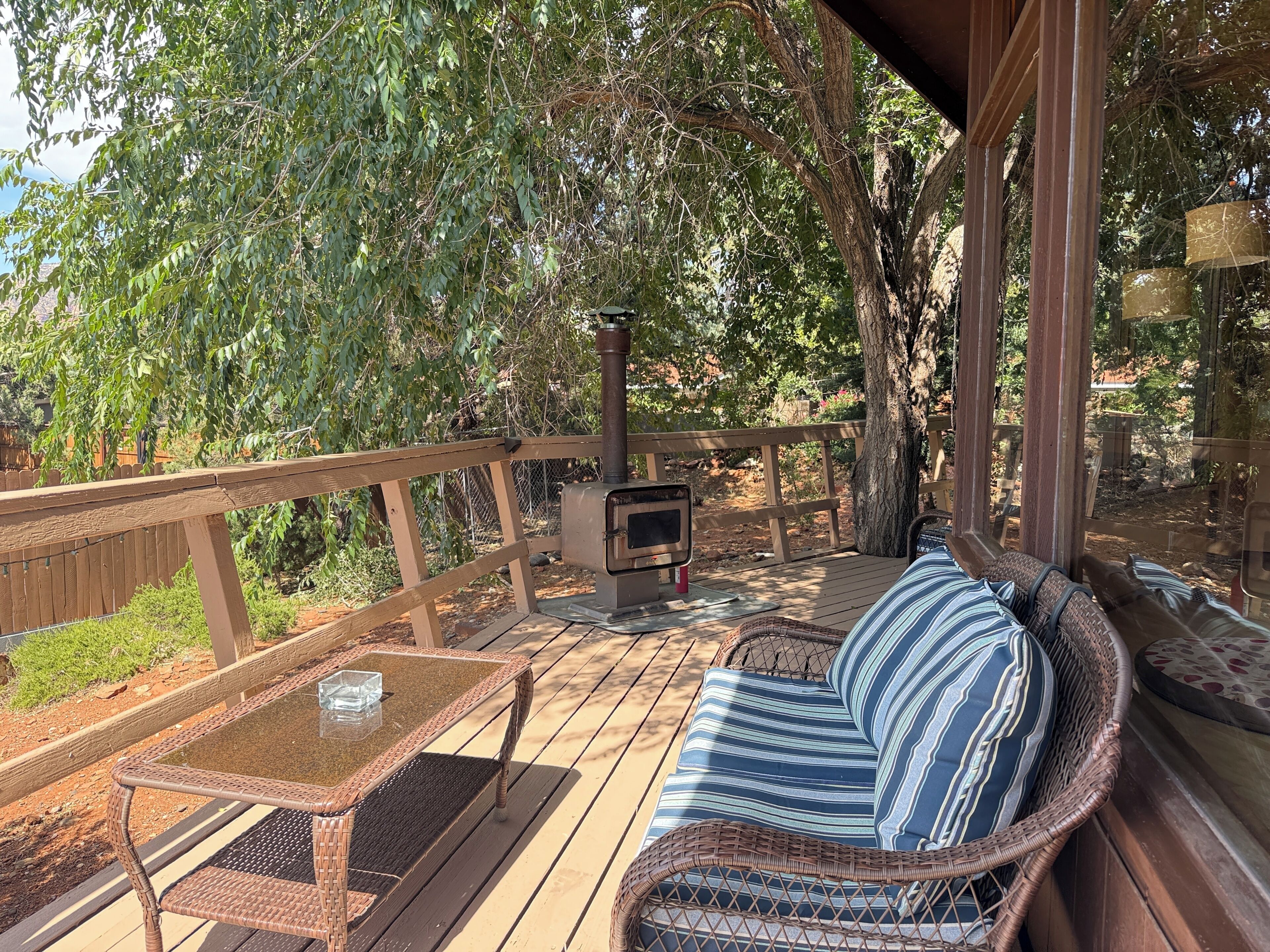 A covered outdoor deck with a wicker sofa, a glass-top table, and a wood-burning stove.