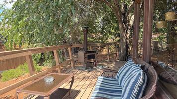 A covered outdoor deck with a wicker sofa, a glass-top table, and a wood-burning stove.