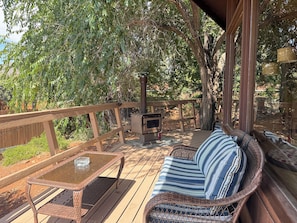 A covered outdoor deck with a wicker sofa, a glass-top table, and a wood-burning stove.