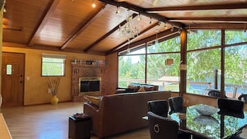A spacious living area with a fireplace, large windows, and a high ceiling.