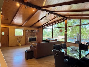 A spacious living area with a fireplace, large windows, and a high ceiling.