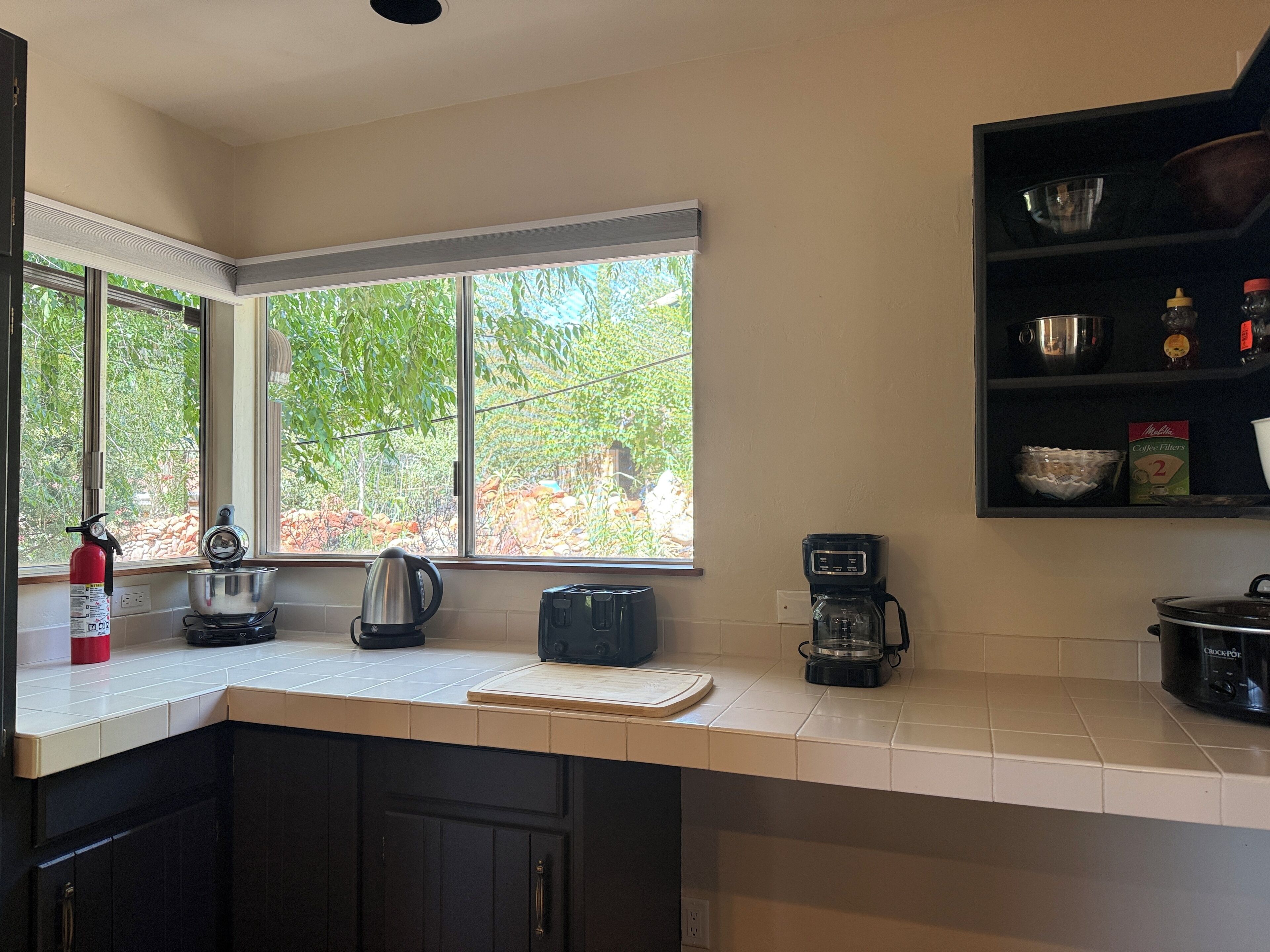 A kitchen with a window, a coffee maker, a kettle, and a stove.