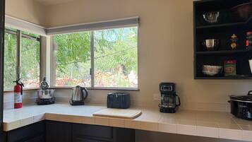 A kitchen with a window, a coffee maker, a kettle, and a stove.