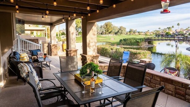 Een overdekt terras buiten met een tafel, stoelen en uitzicht op een golfbaan en een meer.