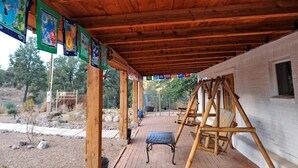 Eine überdachte Terrasse mit Schaukel, Holzbalken und einem weißen Gebäude.