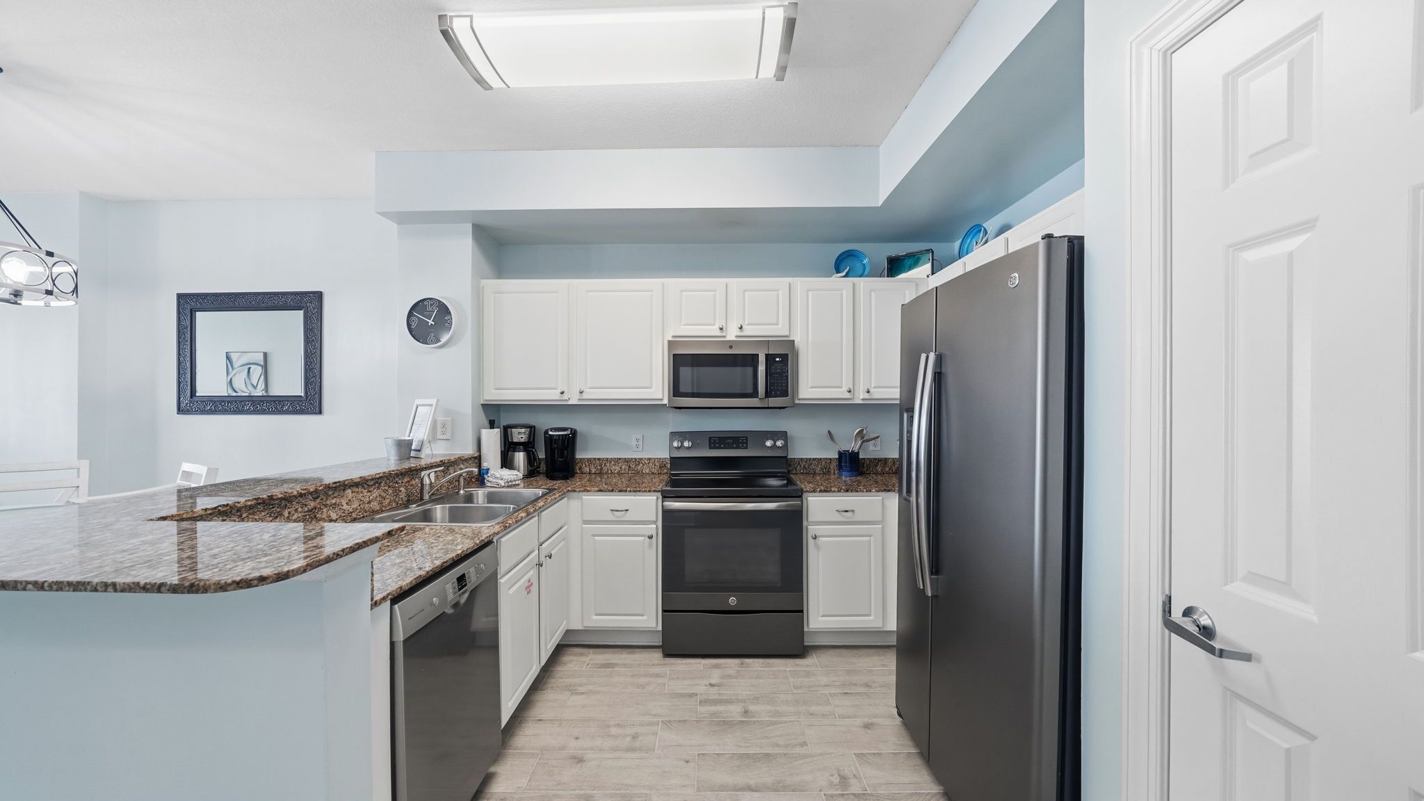 A modern kitchen with white cabinets, a stainless steel refrigerator, a microwave, an oven, and a dishwasher.