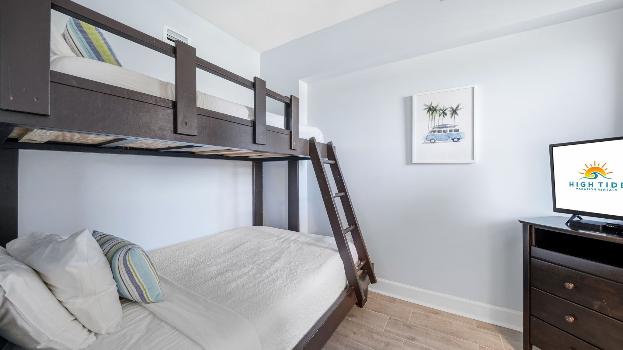 A bunk bed with a ladder, a TV, and a framed picture on the wall.