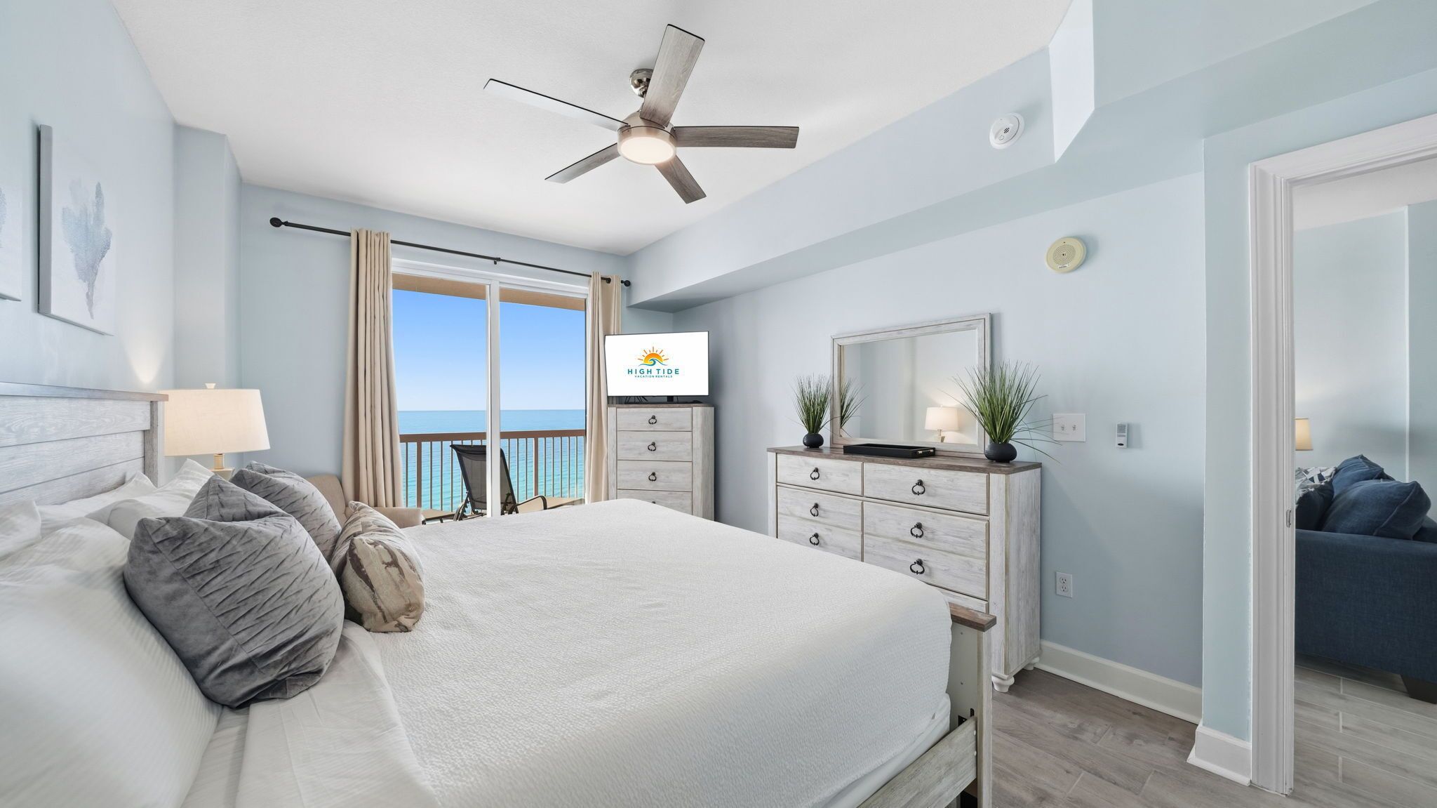 Een slaapkamer met een bed, een dressoir, een plafondventilator en een televisie waarop 'HIGHTIDE' staat.