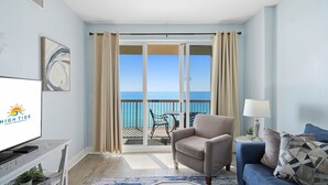 Una habitación con un ventanal grande, un sofá, una silla, un televisor y vista al mar.