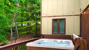 Ein Whirlpool auf einer Holzterrasse mit Holzgeländer, umgeben von Pflanzen und Lichterketten.