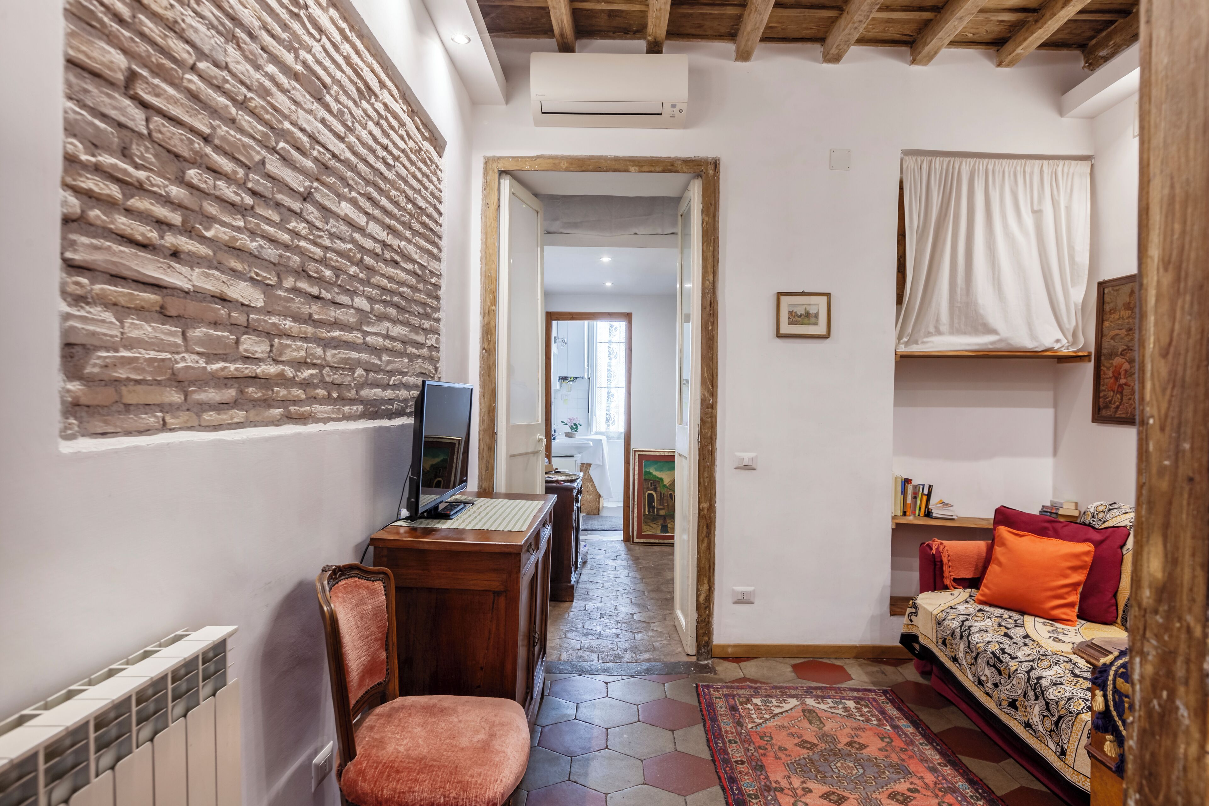 Une pièce chaleureuse avec un mur en briques, un bureau en bois avec un ordinateur, une chaise, un lit avec une literie à motifs et un tapis coloré.