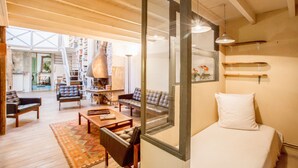 A spacious living area with a large window, wooden ceiling beams, a sofa, a coffee table, and a bed with a white pillow. - Huge loft, full of light, in the lively Canal Saint-Martin, near Marais area (Paris)