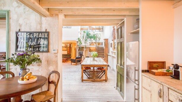 A kitchen with a wooden table, chairs, a vase with flowers, and a sign on the wall. - Huge loft, full of light, in the lively Canal Saint-Martin, near Marais area (Paris)