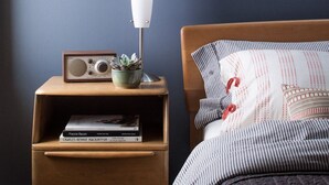 A bedroom with a bed, a nightstand with a radio and books, and a bedside lamp. - PDX Eco Cottage Guesthouse (Portland)