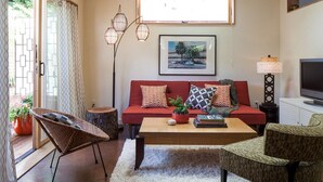 A cozy living room with a wooden ceiling, a red sofa, a coffee table, and a television. - PDX Eco Cottage Guesthouse (Portland)