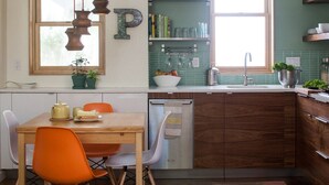 A kitchen with a wooden table, orange chairs, a built-in dishwasher, and a window with a view. - PDX Eco Cottage Guesthouse (Portland)