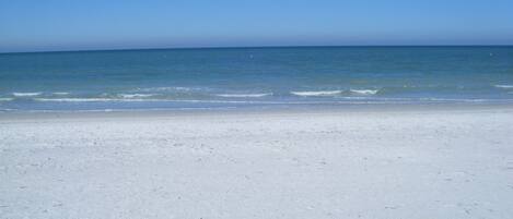 A wide, sandy beach with gentle waves lapping at the shore under a clear blue sky.