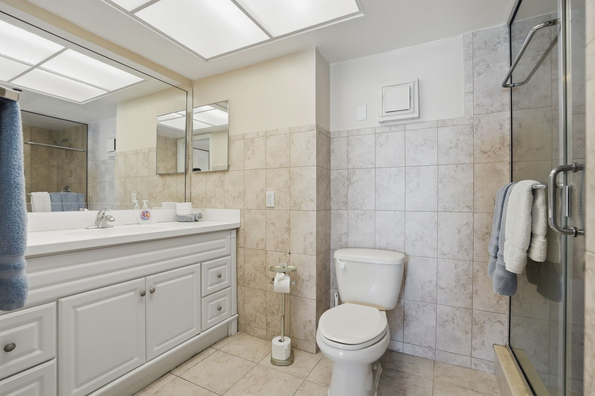 A modern bathroom with a white vanity, a toilet, a shower area, and a large mirror.