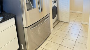 A compact kitchen with a stainless steel refrigerator, a built-in oven, and a washing machine. - Special Nov 14-21, 2026 - IRB Direct Beach Front Corner Condo (Indian Rocks Beach)