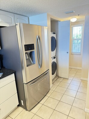 A compact kitchen with a stainless steel refrigerator, a built-in oven, and a washing machine.