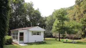 A small white shed with a door and windows, surrounded by a grassy yard and trees. - Walk to White Oak Canyon Trail in Shenandoah National Park (Syria)