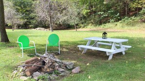 A picnic setup with a white table and two green chairs, surrounded by a natural setting with trees and a pile of logs. - Walk to White Oak Canyon Trail in Shenandoah National Park (Syria)