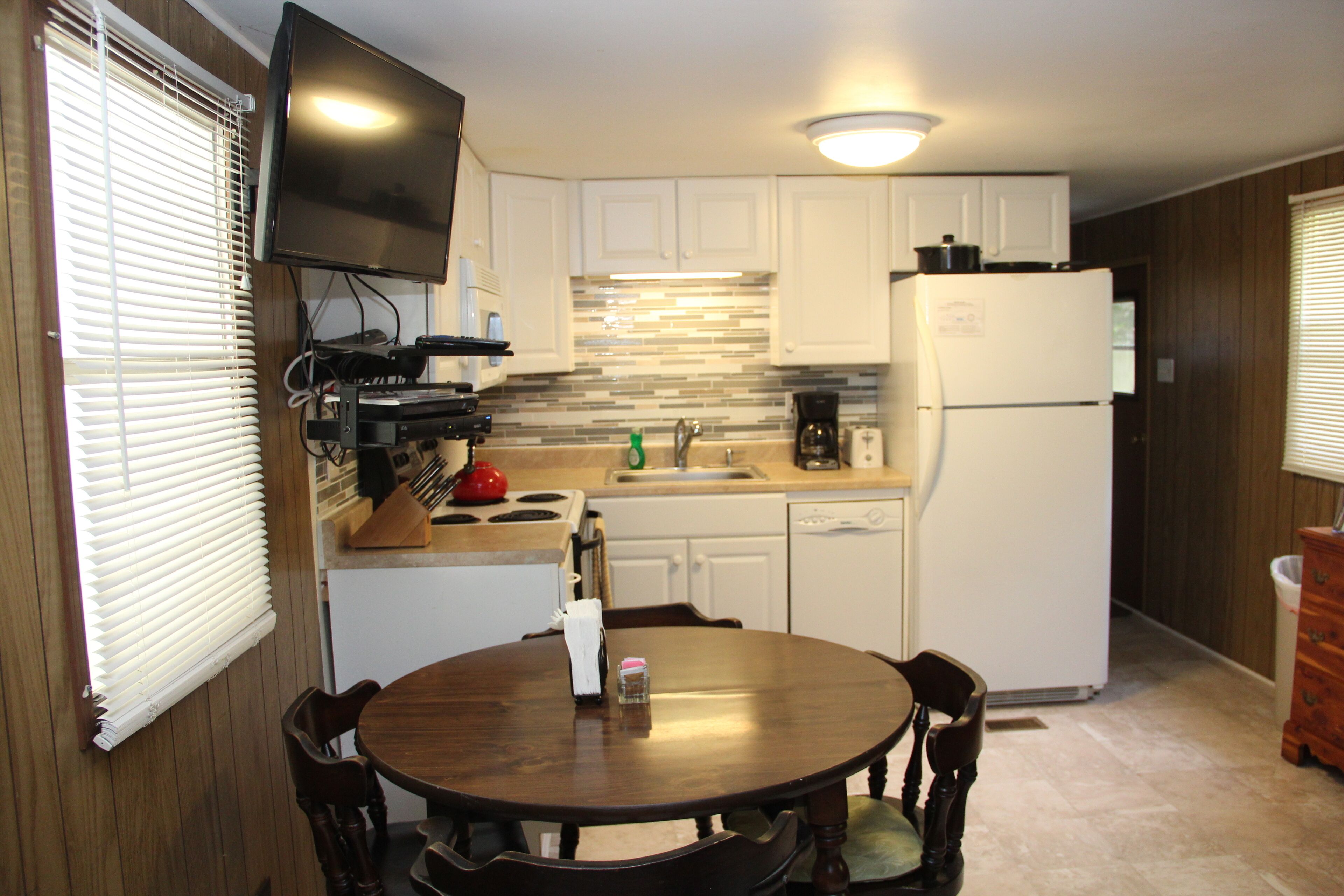 Una cocina compacta con armarios blancos, horno empotrado, refrigerador y una mesa de comedor con cuatro sillas.