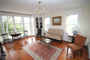 A spacious living room with hardwood floors, a red patterned rug, a sofa, a chair, a table, and a chandelier. - "Old River House", FAMOUS HISTORIC ELEGANCE. Waterfront/Crashing Ocean Sounds  (Kennebunkport)