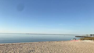 A beach with calm water, a clear sky, and a distant pier.
