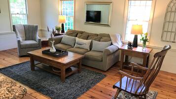 A living room with a sofa, armchair, coffee table, and wooden flooring.
