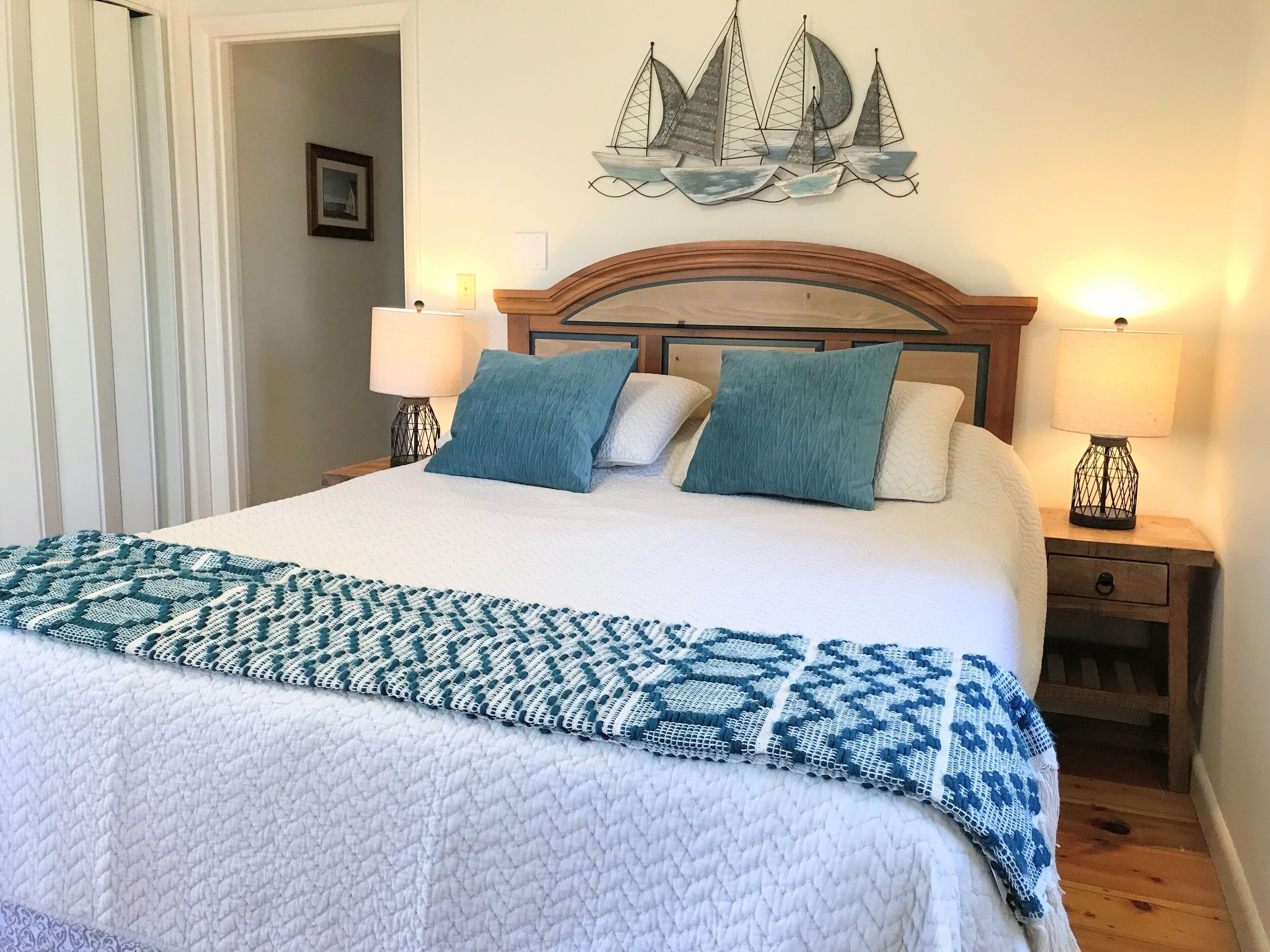A neatly made bed with a patterned blanket, two pillows, and a wall-mounted ship decoration.