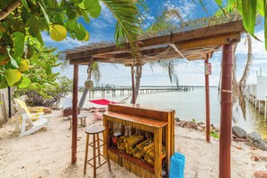 A beach bar with a wooden structure, white chairs, and a view of the water.