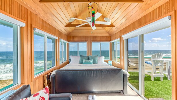 A bedroom with a large bed, wooden ceiling, and a view of the ocean.