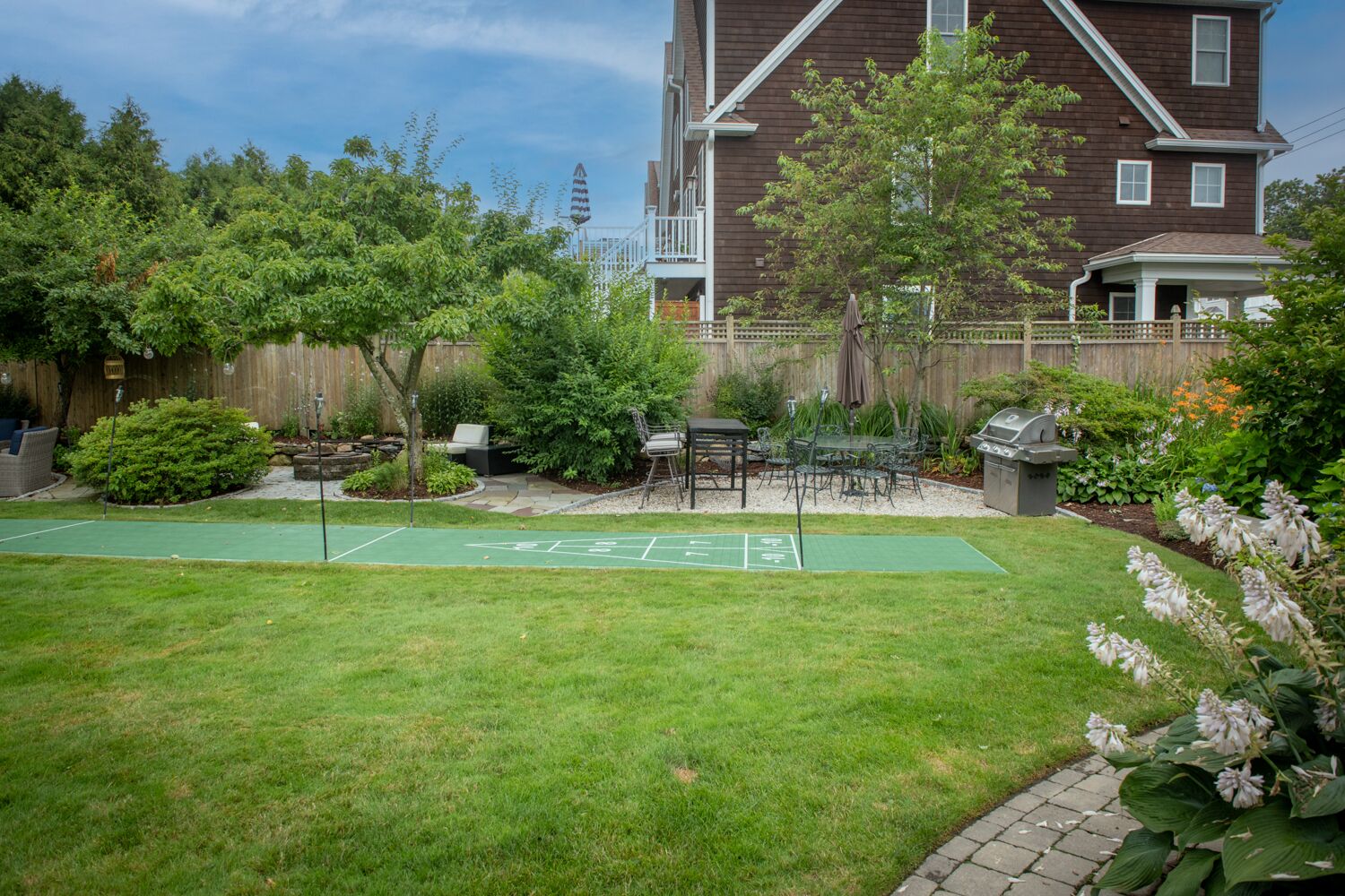 A backyard with a shuffleboard court, a barbecue grill, and a patio area with outdoor furniture.