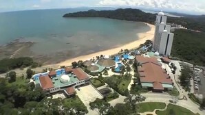 An aerial view of a coastal resort with a beach, a large building with a dome, and a parking area.