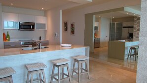 A modern kitchen with a central island, stainless steel appliances, and three wooden stools.