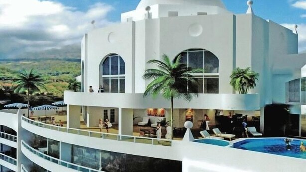 A white building with a dome and arched windows, overlooking a pool area with lounge chairs and palm trees.