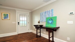 A hallway with a wooden floor, a white door, and a console table with a green painting and a small sculpture.