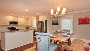 A modern kitchen with white cabinetry, stainless steel appliances, and a wooden dining table with blue chairs.
