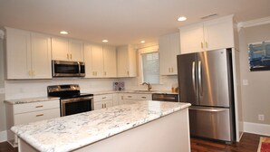A modern kitchen with white cabinets, stainless steel appliances, and a marble countertop.