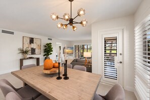 A dining area with a wooden table, chairs, a chandelier, and a door with blinds.